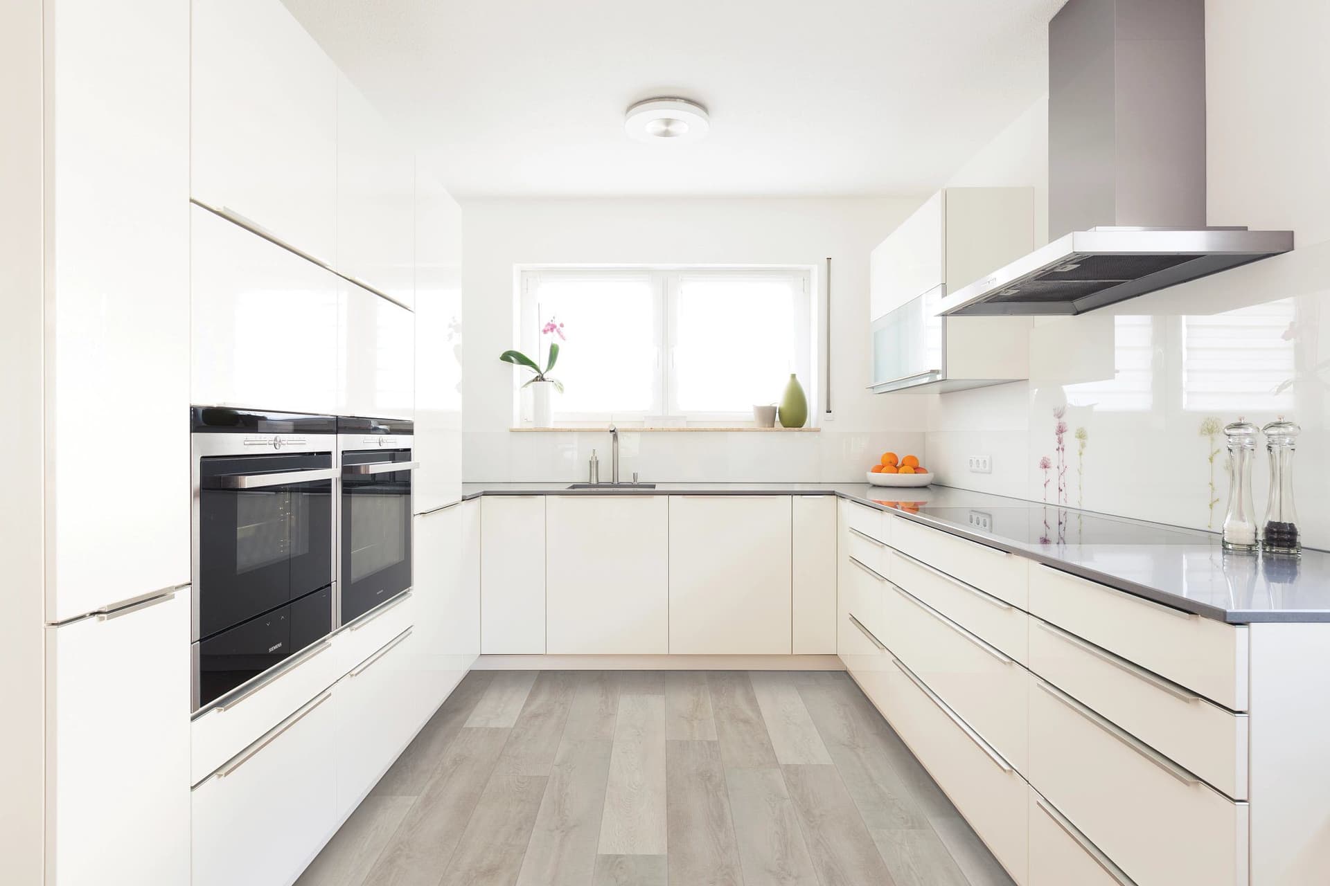 A kitchen with white cabinets and wood floors.