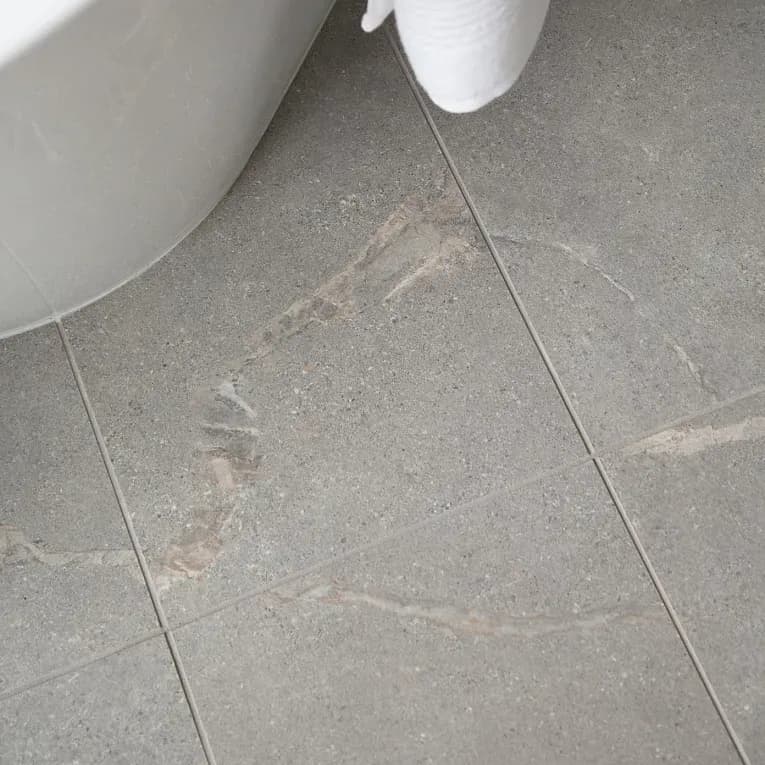 A bathroom floor with a white toilet and gray tile.