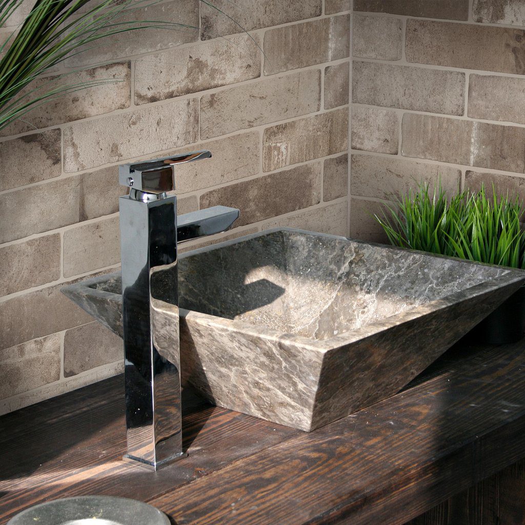 A sink with a metal faucet and a brick wall