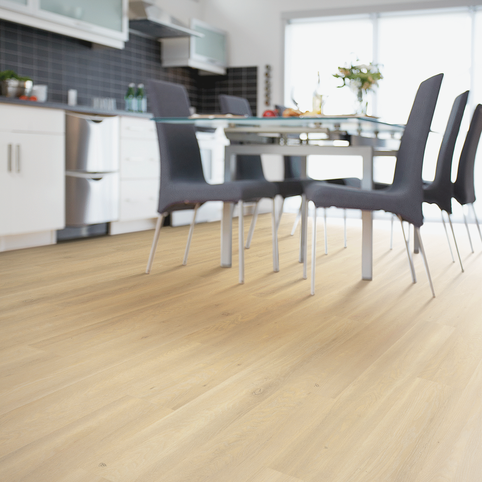 A dining room table and chairs in front of a kitchen.