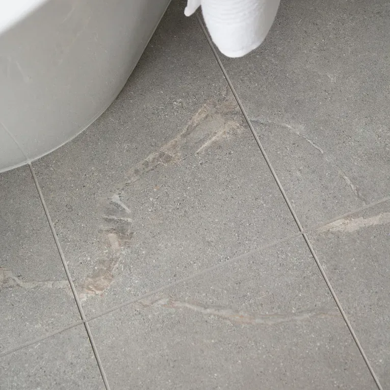 A bathroom floor with a white toilet and gray tile.