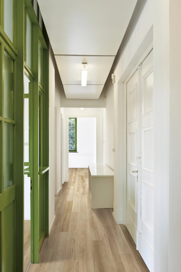 A hallway with green doors and white walls.