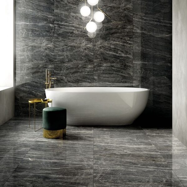 A bathroom with marble walls and floors, a tub, and a gold stool.